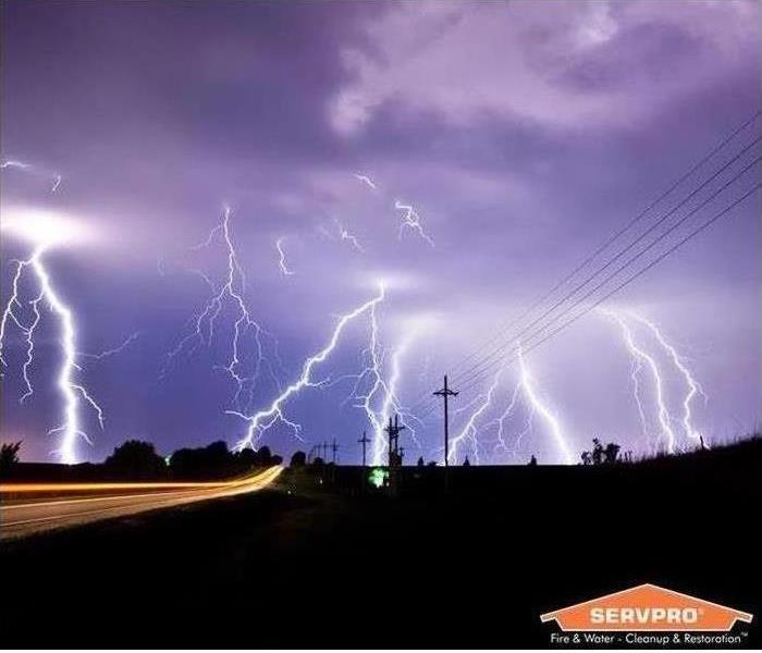 Lightning lights up a open field alongside a highway